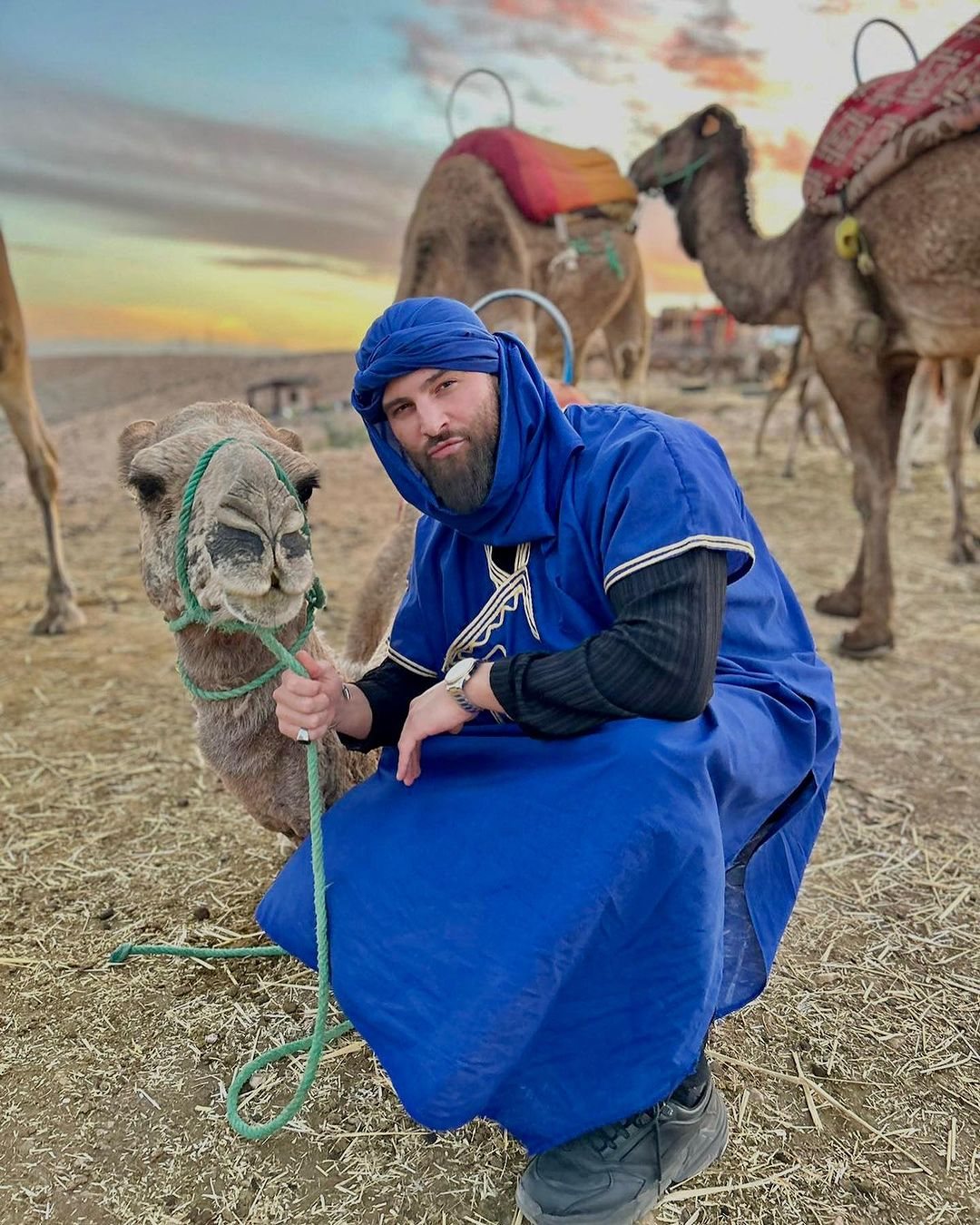 A local man in blue clothing beside a camel