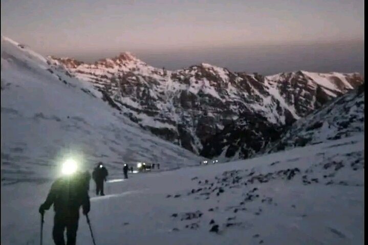 Hikers walking across a snowy mountain before sunrise