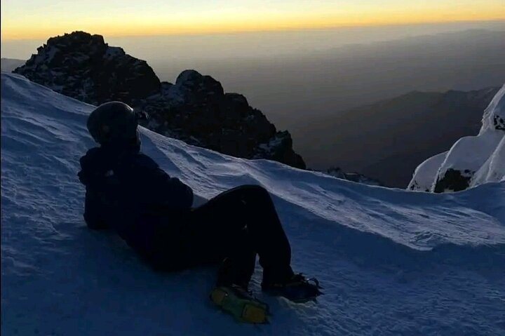 A hiker resting on a snowy mountain slope at sunset